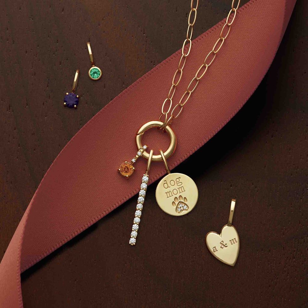 14k gold circle clasp necklace with a 'dog mom' charm, gemstone charms, a diamond bar charm, and a heart charm.